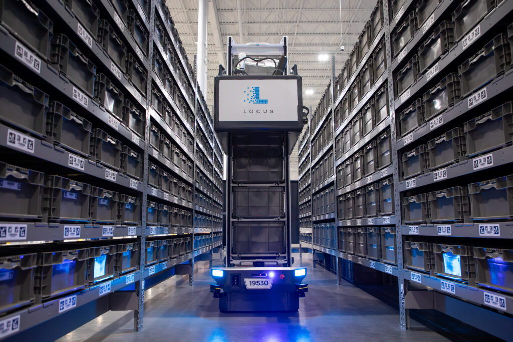 Locus Array robot with a Locus-branded display traveling down a lit aisle of gray storage totes